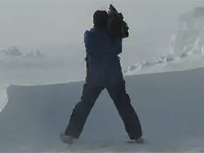 Man with a video camera stands on an icy landscape.