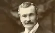 A well-dressed man with a mustache poses confidently in a formal studio portrait from the late 19th or early 20th century.