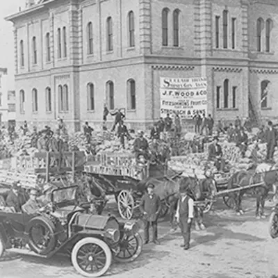 Black and white image of cars, horse and wagons.