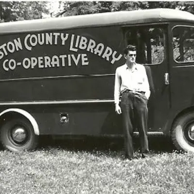 Black and white image of a man standing in front of a van.