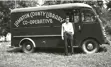 Black and white image of a man standing in front of a van.