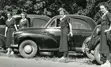 winnifred james among three other women, standing of to the side of the road in front of old cars.