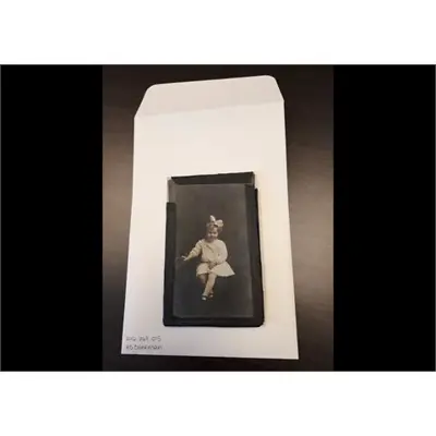 A vintage photograph of a young girl with a large bow in her hair is displayed on an envelope labeled 2016.067.015 4B Clinkman.